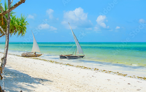 Traditional African solid wood boats under sail on the shore of the Indian ocean with turquoise water on the island of Zanzibar, a concept of travel and summer