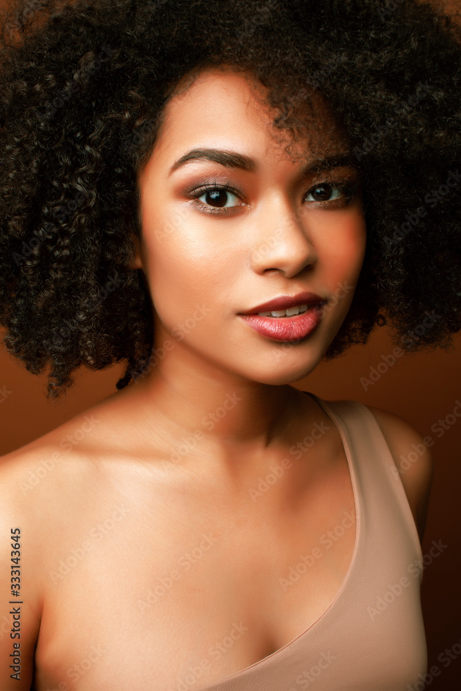 pretty young african american woman with curly hair posing cheerful gesturing on brown background, lifestyle people concept pretty young african american woman with curly hair posing cheerful gesturing on brown background, lifestyle people concept