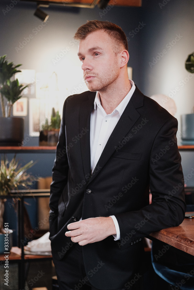 A handsome young bearded man blond in a suit and shirt in a restaurant with a loft interior. He sits at a table, read a magazine. A handsome young bearded man blond in a suit and shirt in a restaurant with a loft interior. He sits at a table, read a magazine.