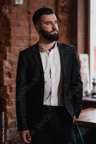 A young handsome man with a beard in a business suit in the interior of a restaurant.