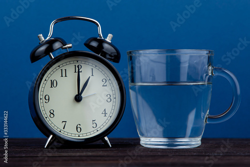 Alarm clock and a glass of water on a blue background. body water balance
