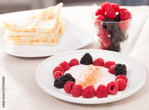 breakfast of raspberries and blackberries with yogurt and pancakes on table