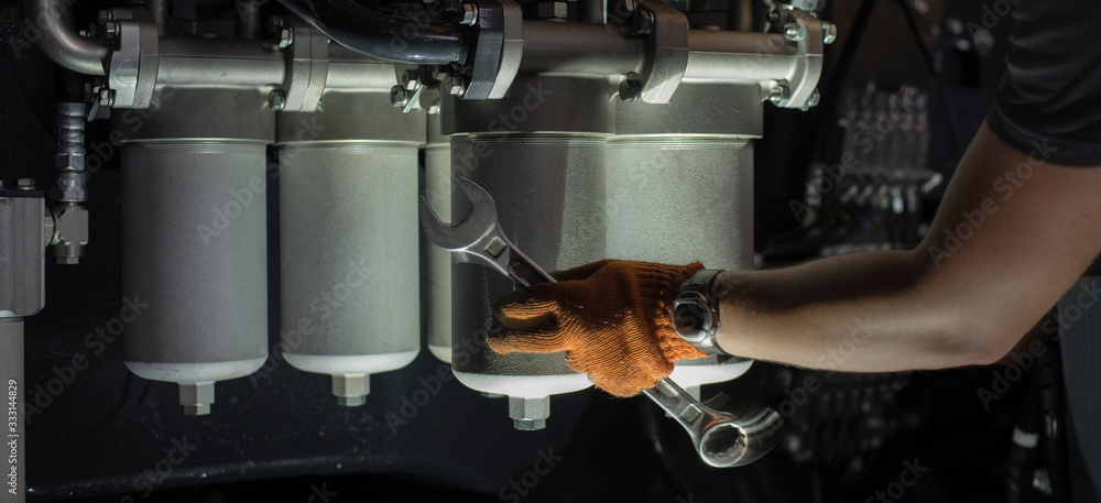 Fototapeta premium Banner with close up view of hydraulic pipes of heavy industry machine and hands of mechanic. Low key.