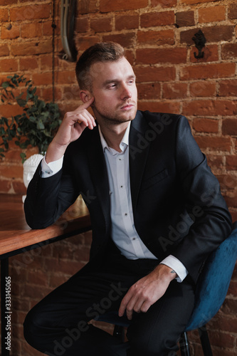 A handsome young bearded man blond in a suit and shirt in a restaurant with a loft interior. He sits at a table, read a magazine.