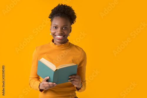 beautiful young african woman on yellow background with a book