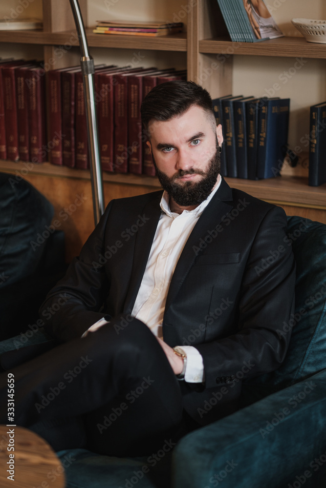 A young handsome man with a beard in a business suit in the interior of a restaurant.