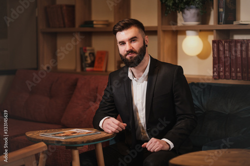 Portrait of a young handsome bearded man. A businessman in a suit sits at a table in a cafe or restaurant.