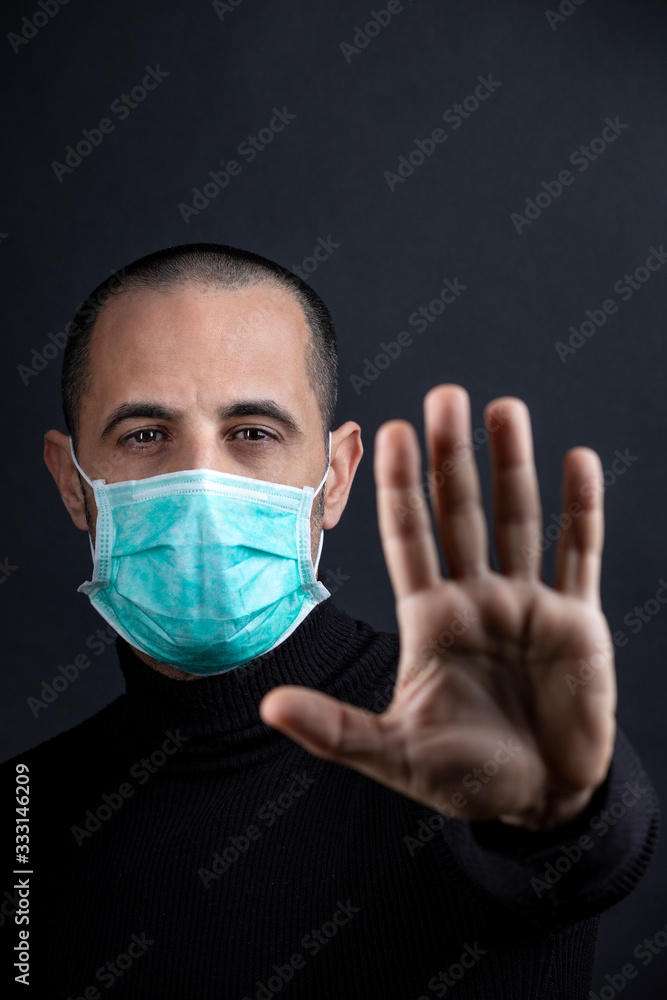 Ragazzo rasato indossa una mascherina chirurgica verde e indica con le mani il segno di stop, isolato su sfondo nero Ragazzo rasato indossa una mascherina chirurgica verde e indica con le mani il segno di stop, isolato su sfondo nero