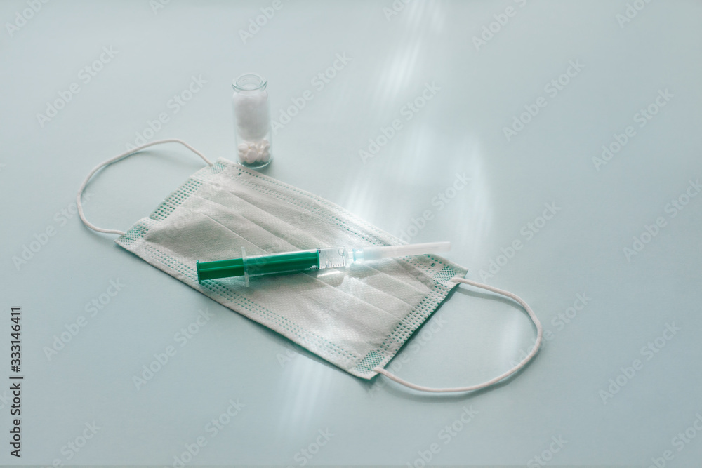A protective mask, a green syringe and a bottle of pills on a blue background. Concept of health protection and prevention of viral diseases. The view from the top, place for text A protective mask, a green syringe and a bottle of pills on a blue background. Concept of health protection and prevention of viral diseases. The view from the top, place for text