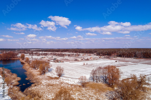 Fototapeta Naklejka Na Ścianę i Meble -  View from above of the countryside and brook on a sunny day. Snowy nature landscape with blue sky. Early spring