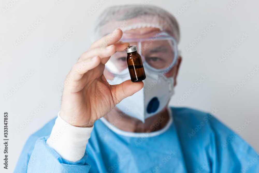 Coronavirus Covid-19 concept. Doctor in glasses and a respirator mask for protection holds a vaccine bottle. Wuhan, China epidemic virus Cov-19 symptoms quarantine background Corona virus outbreaking. Coronavirus Covid-19 concept. Doctor in glasses and a respirator mask for protection holds a vaccine bottle. Wuhan, China epidemic virus Cov-19 symptoms quarantine background Corona virus outbreaking.