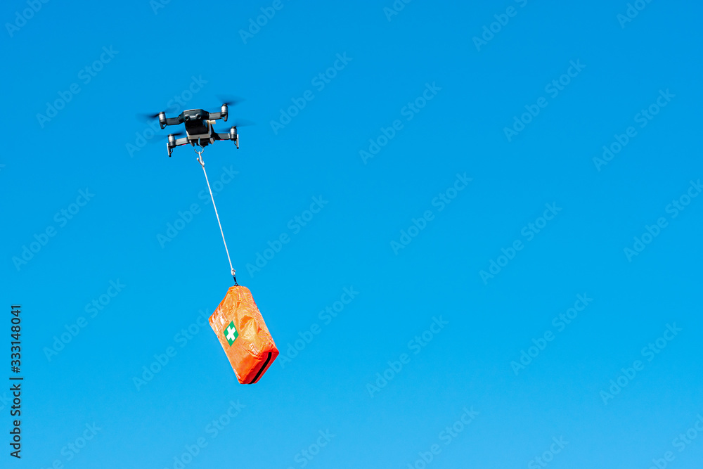 multicopter drone flying with a first aid kit isolated on a blue sky, emergency medical care concept multicopter drone flying with a first aid kit isolated on a blue sky, emergency medical care concept
