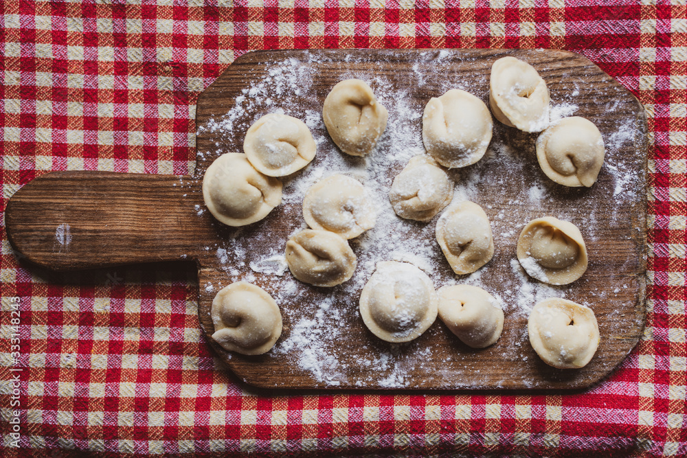 Making pelmeni, dumplings of Russian and Eastern European cuisine on a board with flour, ready to be boiled