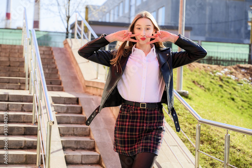 Spring vertical photo of a happy smiling beautiful girl with emotions in the sun outdoors on the background of the steps in the city. Pretty model posing with hands on camera. photo