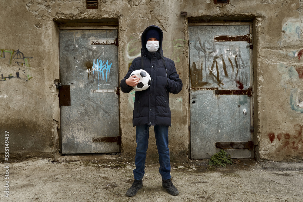 concept of epidemic and quarantine - a boy with a face mask and a ball alone on the street in the city