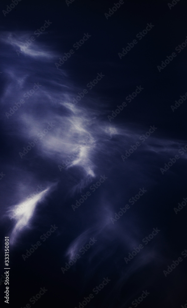 A white cirrus cloud resembling a bird's feather against a dark blue sky. Vertical photography