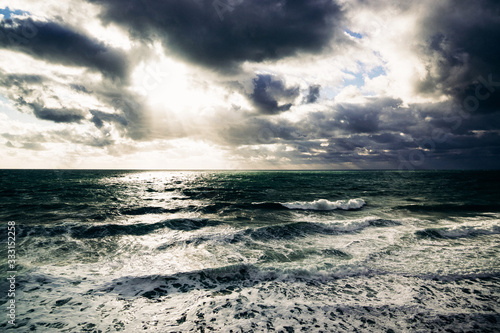 Fototapeta Naklejka Na Ścianę i Meble -  White sunlight breaks through storm clouds into the raging green sea water