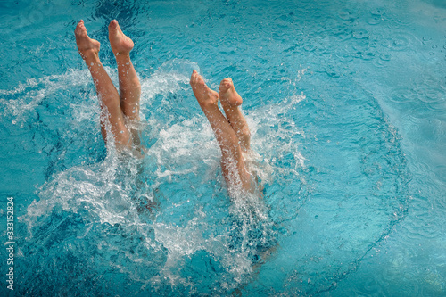 Obraz na płótnie Legs of synchronized swimmers girls peeking out of the pool water in a show perf