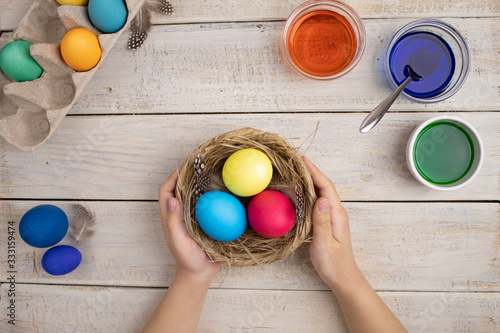 Child's hands holding brown nest with Easter eggs on white background. Concept of Happy Easter .