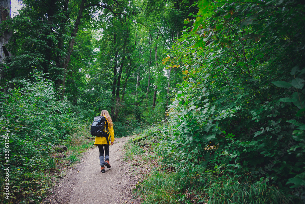 Hiker girl on a trail in the forest wearing yellow jacket and backpack Hiker girl on a trail in the forest wearing yellow jacket and backpack