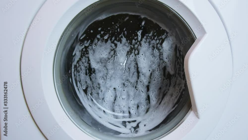 Washing clothing in generic domestic washing machine.Close up video of spinning washing machine drum with foam spraying door. Washing clothing in generic domestic washing machine.Close up video of spinning washing machine drum with foam spraying door.