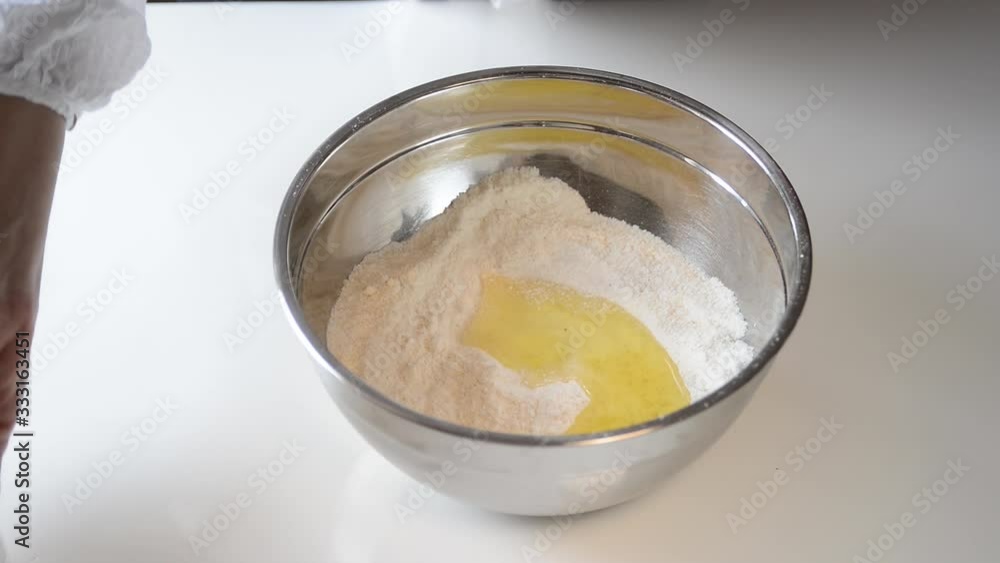 Baker prepares dough with eggs, sugar and flour in a bowl on a white table. Woman mixing ingredients for making cookies. Baker prepares dough with eggs, sugar and flour in a bowl on a white table. Woman mixing ingredients for making cookies.