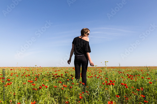 backview of girl in black staying in wild red poppy fower field in spring time near Almaty, Kazakhstan