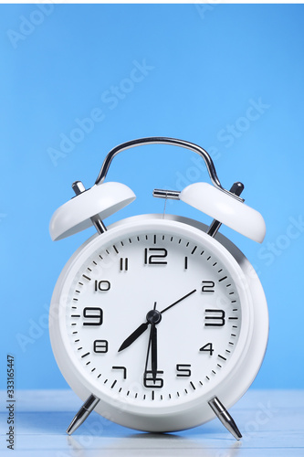 white retro alarm clock on the wooden table on a blue background