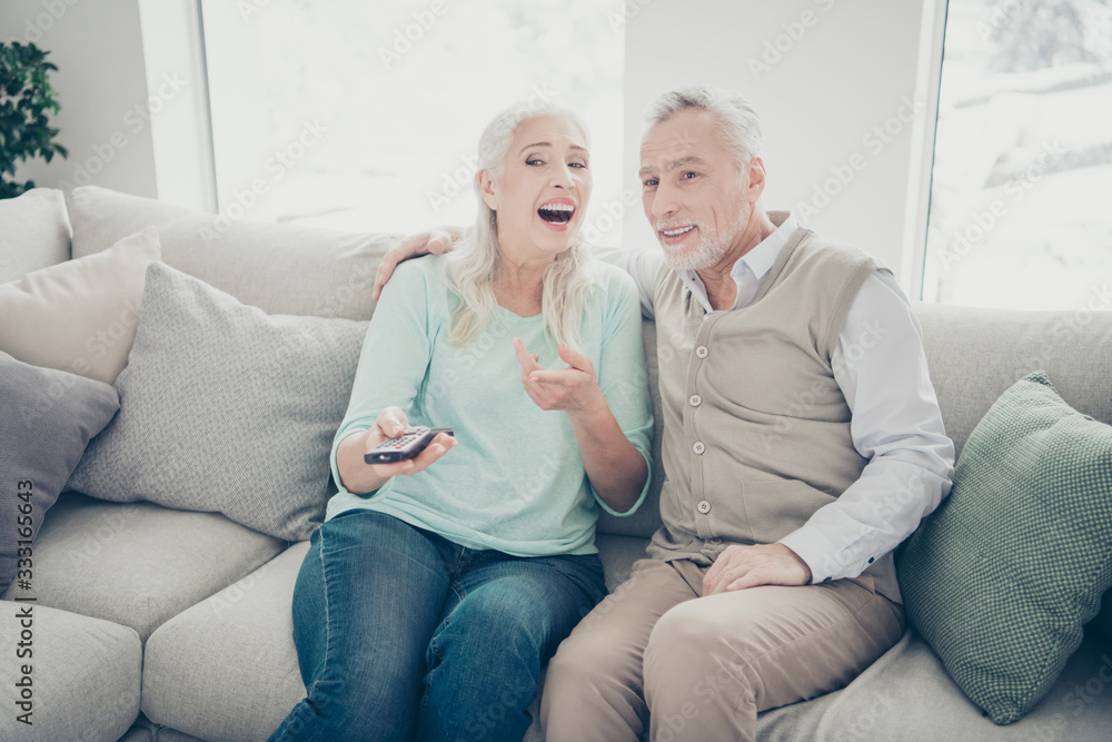 Photo of two aged people pair spending free time together watching humorous serial sitting cozy sofa