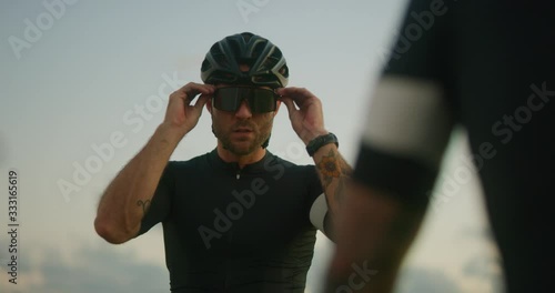 Road cyclist puts sunglasses on preparing to ride at sunset