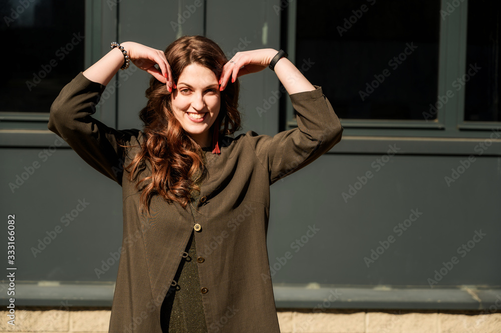 Photo of a pretty fashionable happy brunette woman with long beautiful hair with a smile in a suit on the background of the steps of the building in sunny weather Photo of a pretty fashionable happy brunette woman with long beautiful hair with a smile in a suit on the background of the steps of the building in sunny weather