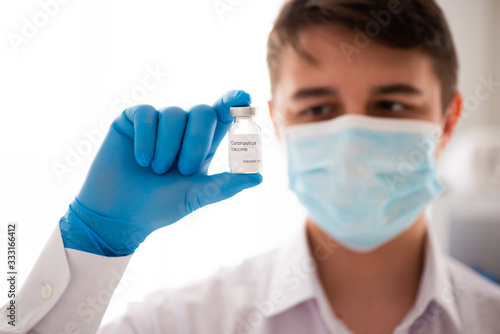 Vaccine bottle in male hand close up, doctor in medical mask. Concept of vaccination, Covid-19 coronavirus diagnostic, cure for the flu virus