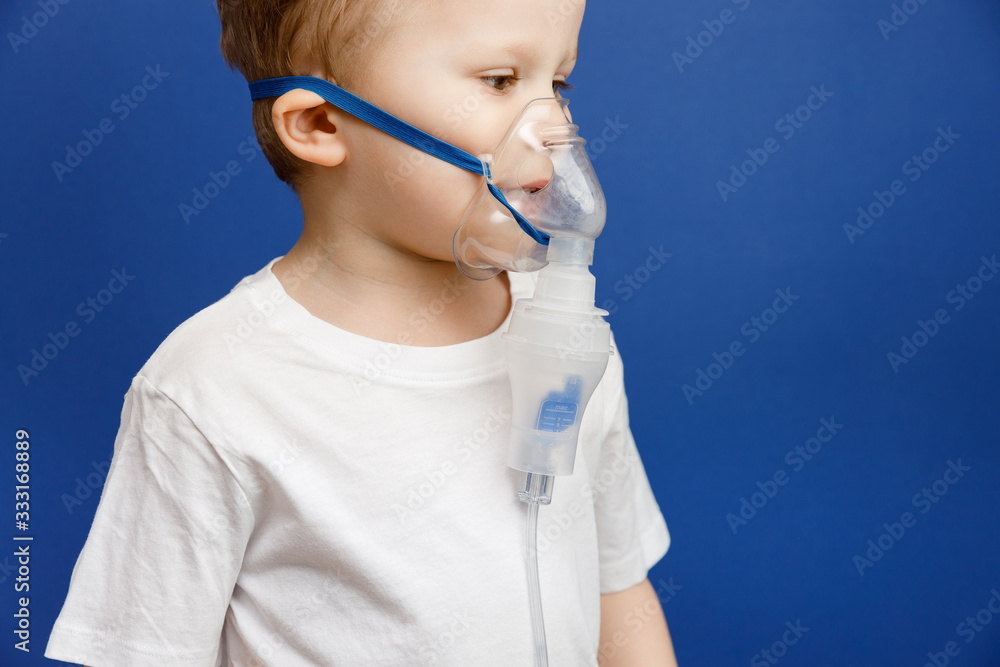 The boy wearing breathing face mask against flu or coronavirus infection. Inhaler or nebulizer equipment. Banner panorama medical preventive gear on blue background. The boy wearing breathing face mask against flu or coronavirus infection. Inhaler or nebulizer equipment. Banner panorama medical preventive gear on blue background.