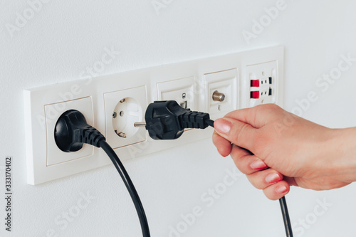 A female hand is pulling an electrical cord plugged into a socket