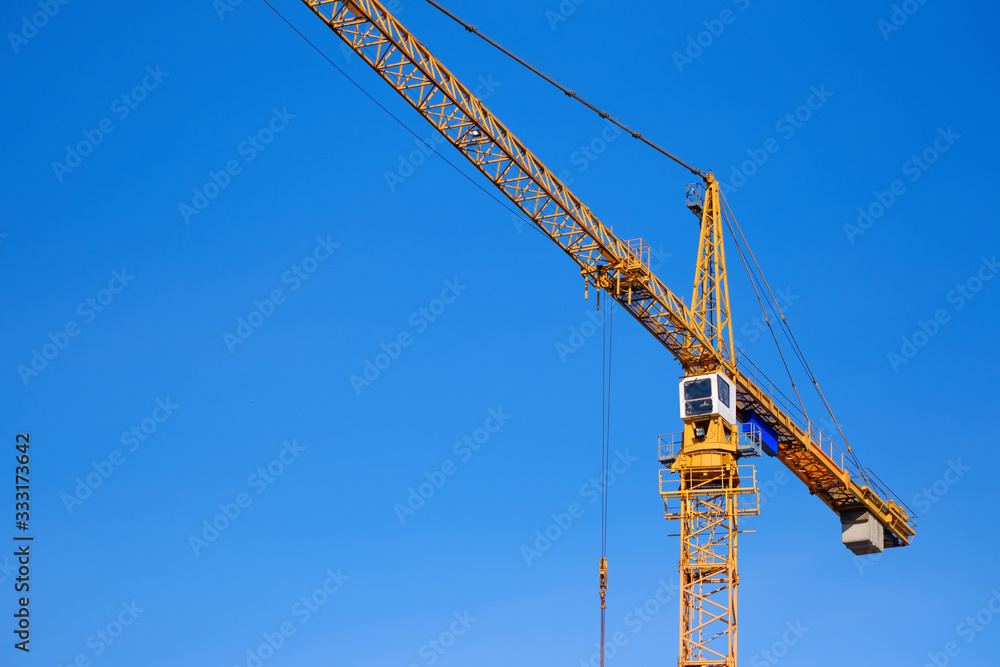 Construction crane against blue sky background. Yellow hoisting crane. Industrial construction. Copy space Construction crane against blue sky background. Yellow hoisting crane. Industrial construction. Copy space