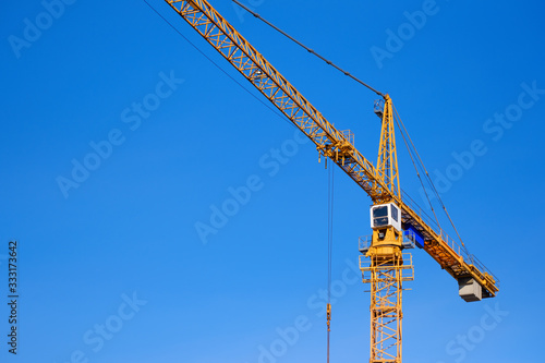 Construction crane against blue sky background. Yellow hoisting crane. Industrial construction. Copy space