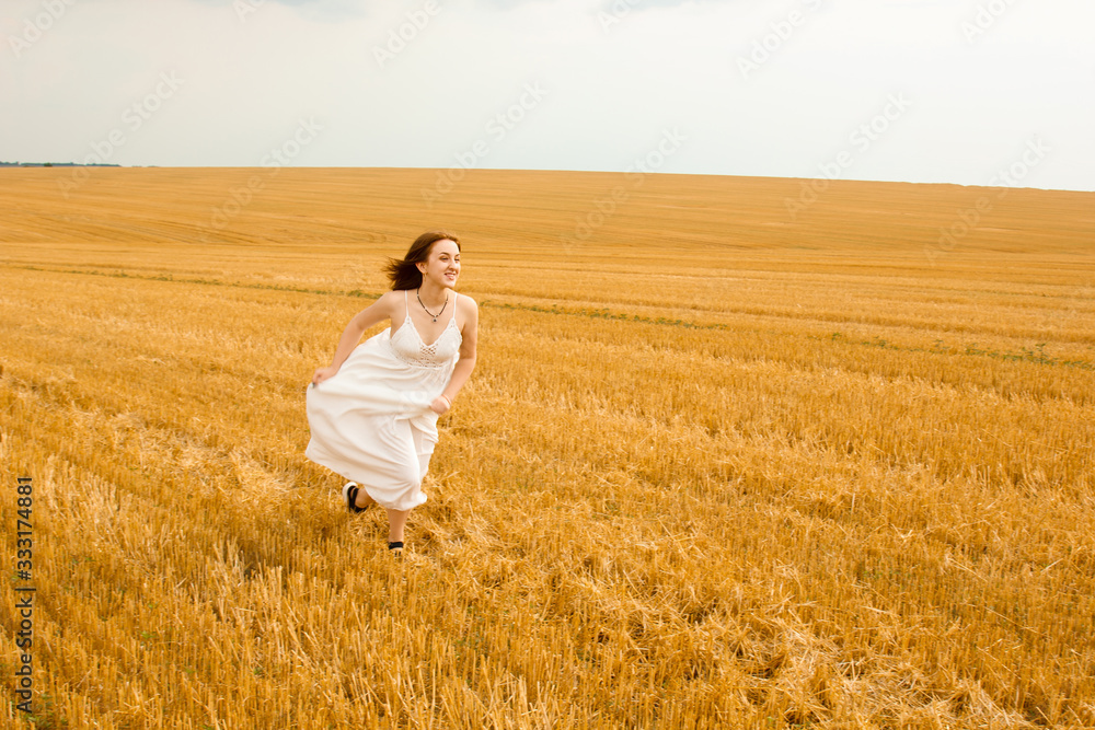 Runs across the field. Young beautiful redhead woman in the middle of a wheat field having fun. Summer landscape, good weather. Windy day with the sun and clouds. White cotton dress, eco style. Runs across the field. Young beautiful redhead woman in the middle of a wheat field having fun. Summer landscape, good weather. Windy day with the sun and clouds. White cotton dress, eco style.