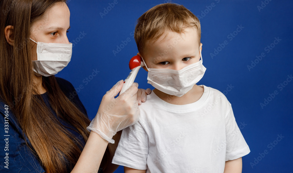 Doctor or nurse takes the temperature of a small boy. Personal protective equipment against viruses and infections. Flu or coronavirus symptoms.
