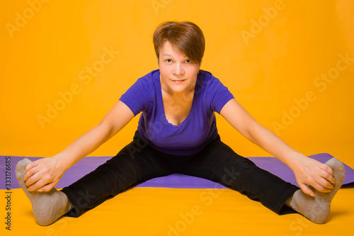 Aged woman doing yoga on a purple rug. Studio photo on a yellow background.