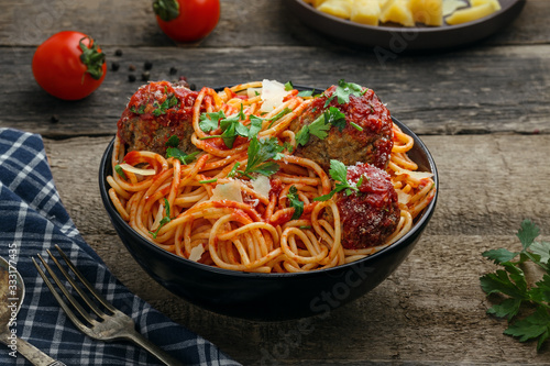 Traditional Italian spaghetti with meatballs and parmesan in tomato sauce in a black bowl. American family meal on a table.