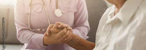 Fotografie Young doctor holding hand of elderly woman on light background