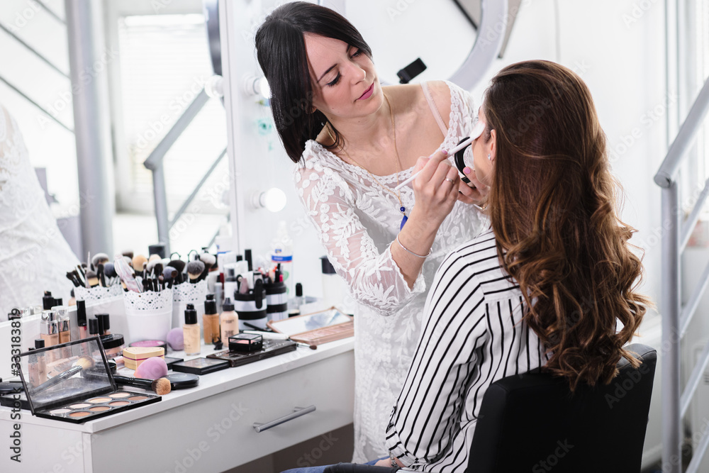 Young female make-up artist applying makeup on model in beauty salon. Young female make-up artist applying makeup on model in beauty salon.