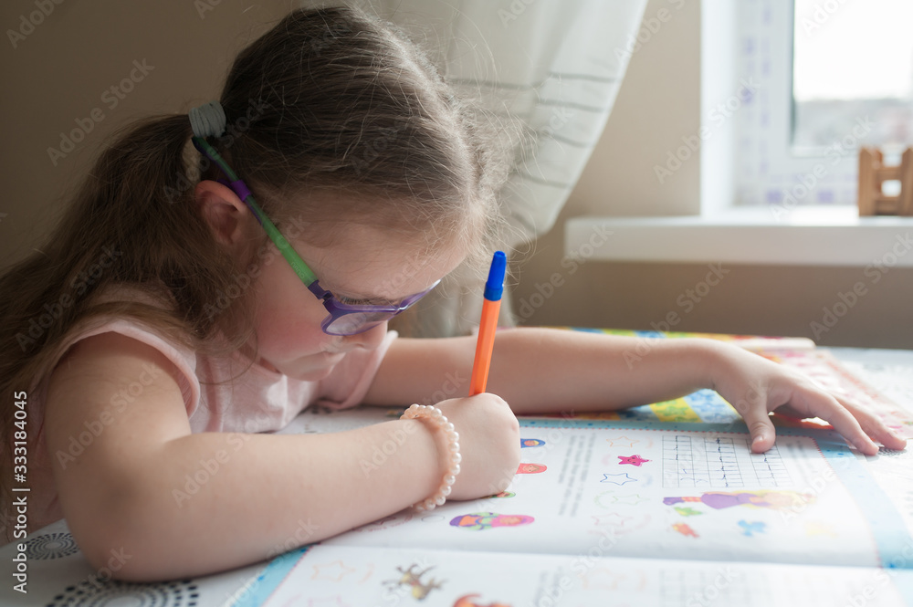 Happy pretty child girls sitting at the table and writes. Educational activities at home. Distance learning. Girl with glasses. Vision problems