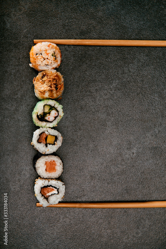 Stock photo of maki sushi stacked between two chopsticks with black background.