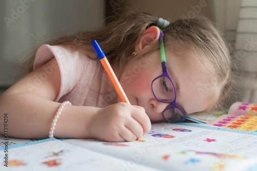 Happy pretty child girls sitting at the table and writes. Educational activities at home. Distance learning. Girl with glasses. Vision problems photo