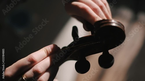 Young woman fiddler changing violin strings, tighten the string with the tuning peg at pegbox, moody low light scene at home