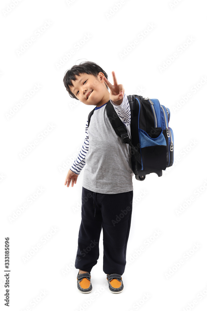 Fototapeta premium A cheerful Asian primary schoolboy with a backpack showing victory gesture sign isolated on white background.