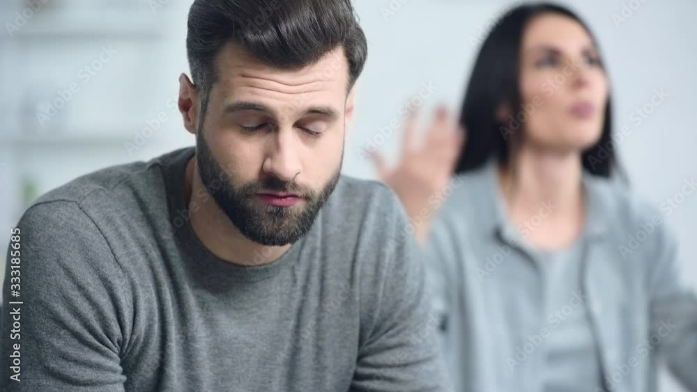 selective focus of man sitting near displeased girlfriend selective focus of man sitting near displeased girlfriend