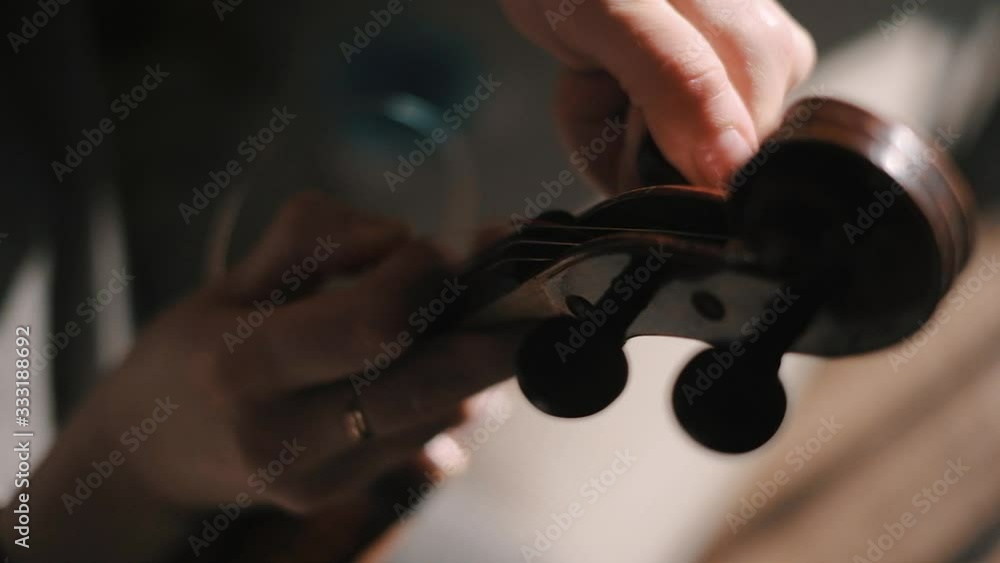 Young woman fiddler changing violin strings, tighten the string with the tuning peg at pegbox, moody low light scene at home Young woman fiddler changing violin strings, tighten the string with the tuning peg at pegbox, moody low light scene at home