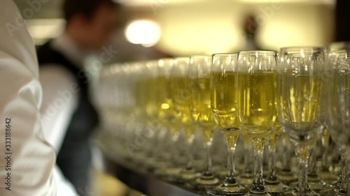 On the table is a large number of glasses of champagne, in the background you can see the waiters in white shirts and black vests, close-up, slow-motion shooting